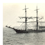 Black and white photograph of a masted ship at sea.